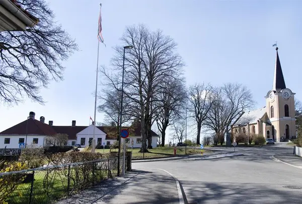 Til venstre i bildet ser vi et hvitt gammelt murbygg. Til høyre ser vi en hvit kirke, også i mur. Det er vinter og sol, trærne er bare