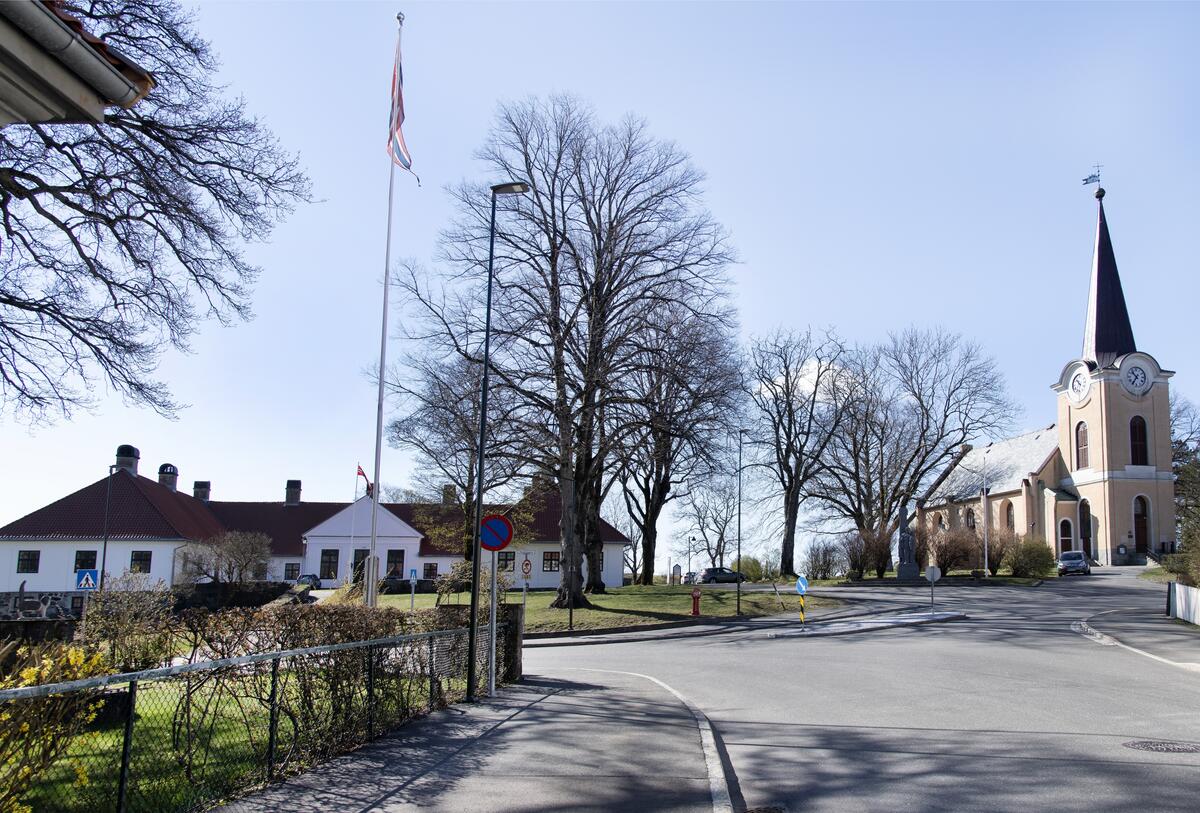 Til venstre i bildet ser vi et hvitt gammelt murbygg. Til høyre ser vi en hvit kirke, også i mur. Det er vinter og sol, trærne er bare