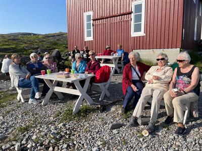 Flere mennesker i solveggen til naustet på Fuglenesodden Friluftsmuseum.