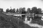 Motiv från Linköpings hamnområde i höjd med Nykvarnsparken. Året är 1892 och vid kaj ses bogserångfartyget Tekla, byggd i Stockholm 1889 för trafik på Kinda kanal. Fartyget tillhörde P. Wikström i Stockholm som även ägde Linköpings ångsåg vars anläggningar skymtar mellan träden i bakgrunden.