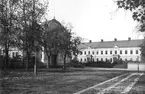 Vy över planen framför Linköpings domkyrka med blicken vänd mot nordväst. Till vänster gymnastikhuset till stadens läroverk, uppfört under åren 1880-81. I fonden den så kallade Konsistoriegården med säte för domkapitlet. Husets östra del uppfördes ursprungligen som skolbyggnad, så kallad trivialskola, under 1820-talets senare del. Tidigare skall här legat ett äldre stenhus, vars grundmurar i delar bär upp huset. I sin år 1834 utgivna 