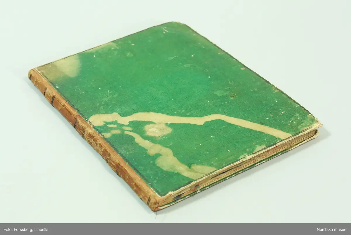 Inbunden bok med gröna pärmar och brun skinnrygg. Innehåller  11 sidor med  267 inklistrade tygprover, daterade från 1824-1858. Det är prov på främst klänningstyger använda  av kvinnorna i familjen Roos af Hjelmsäter bosatta på Rosenbergs malmgård vid Hornskroken i Stockholm, sannolikt mest från  Jeanette Wilhelmina f. 1808, gift 1843 och död 1863 . Proverna är grupperade kronologiskt, klistrade eller fastsatta med rött lack. Det är en blandning av hemvävda bomulls- och halvlinnetyger, smårutiga eller med smala mönstrade bårder av den typ som var modernt under 1820-30-talet, och bomullsripstyger med mönstrade blombårder i silke, ofta kallade västtyger, samt småmönstrade sidentyger sannolikt fabriksvävda.
68 sidenprover, 27 halvsiden, 1 tryckt siden, 64 bomullstyger, 62 tryckt bomull, 1 bolstervarstyg, bomull, 17 halvylle, 14 tryckt helylle, 2 helylle, 5 tryckt halvylle 1 linneprov, 1 sammetsprov.
 Från 1824 finns ett vitt sk. sticktyg i bomull som är en importvara. Redan bland de första sidorna från 1820-talet finns flera maskintryckta bomullstyger, vilket återkommer från varje tid och visar hur modet för tygtryck förändrades. Från 1825 och 1828 finns en mängd sidentyger  med småfiguriga mönster en del antagligen jacquardvävda. 1828 finns även en typ av tunna mönstervävda ylletyger med tryckta blommönster. 1833 prover på tunn yllemuslin med tryckta blommönster. Samt 2 prover på vita tunna maskinvävda bomullsmusliner av den typ som sannolikt importerades från England och Skottland och började spridas just kring 1830. Från 1840-talet finns inga prover.  Från 1856 finns flera jacquardvävda sidentyger och tryckta yllemusliner på både vit, svart och ljusgrön botten, dessutom enfärgade släta redgarnsylletyger från 1850-talet . Längst bak i boken skrivet: "Små profver å tyger begagnade i familjen från år 1824 till 1858.  Sophie Lagerberg" . Hon var född 1846, dotter till Jeanette Wilhelmina Roos af Hjelmsäter som tillsammans med maken Carl Julius Lagerberg var bosatt på Rörstrands porslinsfabriks område där han var anställd. Tygerna bör alltså vara prover på vad en välbärgad stockholmskvinna hade i sin garderob.
I boken finns även inklistat en vävnota med tillhörande tygprov på ett bomullstyg i tuskaft med små stiliserade blombårder vävda på 8 skaft och 5 trampor. Påskrift: Arbetat af J.W. Roos af Hjelmsäter på 1820-talet. Detta prov och flera av de andra tidiga i boken hör till den sort som lärdes ut av familjen Ekenmark på deras vävkurser på 1820-talet. Sannolikt hade Jeanette Wilhelmina deltagit i en sådan, och hon ägde också ett ex. av Ekenmarks Wäfmönsterbok. prover i boken finns  på "engelskt klädningstyg med bård af wäfda weck och faconer, stjerntyg på tvären samt mönsterbårderna nr 22, 23, 27, 35 och 37 1/2 i Mönsterbok för Unga Fruntimmer av M.C Ekenmark, samt mönstren 44, 46, 50, 51, 52 i Wäfmönsterboken. 
Att det inte finns några prover från 1840-talet kan bero på att hon då var nygift och hade småbarn och kanhända inte hann med längre. Längst bak i boken har hon klistrat in en vers hon fått av sin egen mor Sofia Gustafva RaH född Bratt från Sunne i Värmland julafton 1824:"Var glad och lycklig nu/ Din glädje tid är när:/ haf Gud i minne Du/ så blir han dig alltid kär./Gud gif dig alt gått och all god hälsa/ så wet jag att jag har bjudit til/ att skaffa dig all lärdom som i/ en god mors magt har stått/ och kom alltid ihåg hvad/ jag har med all godhet lärt dig. /Mamma d. 24 dec. 1824.
Jfr med tygprovsamling 91.897
/Berit Eldvik 2011-02-03