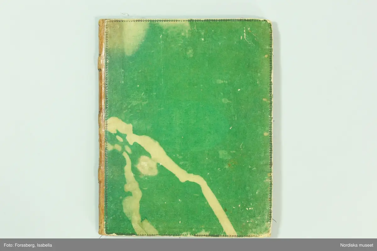 Inbunden bok med gröna pärmar och brun skinnrygg. Innehåller  11 sidor med  267 inklistrade tygprover, daterade från 1824-1858. Det är prov på främst klänningstyger använda  av kvinnorna i familjen Roos af Hjelmsäter bosatta på Rosenbergs malmgård vid Hornskroken i Stockholm, sannolikt mest från  Jeanette Wilhelmina f. 1808, gift 1843 och död 1863 . Proverna är grupperade kronologiskt, klistrade eller fastsatta med rött lack. Det är en blandning av hemvävda bomulls- och halvlinnetyger, smårutiga eller med smala mönstrade bårder av den typ som var modernt under 1820-30-talet, och bomullsripstyger med mönstrade blombårder i silke, ofta kallade västtyger, samt småmönstrade sidentyger sannolikt fabriksvävda.
68 sidenprover, 27 halvsiden, 1 tryckt siden, 64 bomullstyger, 62 tryckt bomull, 1 bolstervarstyg, bomull, 17 halvylle, 14 tryckt helylle, 2 helylle, 5 tryckt halvylle 1 linneprov, 1 sammetsprov.
 Från 1824 finns ett vitt sk. sticktyg i bomull som är en importvara. Redan bland de första sidorna från 1820-talet finns flera maskintryckta bomullstyger, vilket återkommer från varje tid och visar hur modet för tygtryck förändrades. Från 1825 och 1828 finns en mängd sidentyger  med småfiguriga mönster en del antagligen jacquardvävda. 1828 finns även en typ av tunna mönstervävda ylletyger med tryckta blommönster. 1833 prover på tunn yllemuslin med tryckta blommönster. Samt 2 prover på vita tunna maskinvävda bomullsmusliner av den typ som sannolikt importerades från England och Skottland och började spridas just kring 1830. Från 1840-talet finns inga prover.  Från 1856 finns flera jacquardvävda sidentyger och tryckta yllemusliner på både vit, svart och ljusgrön botten, dessutom enfärgade släta redgarnsylletyger från 1850-talet . Längst bak i boken skrivet: "Små profver å tyger begagnade i familjen från år 1824 till 1858.  Sophie Lagerberg" . Hon var född 1846, dotter till Jeanette Wilhelmina Roos af Hjelmsäter som tillsammans med maken Carl Julius Lagerberg var bosatt på Rörstrands porslinsfabriks område där han var anställd. Tygerna bör alltså vara prover på vad en välbärgad stockholmskvinna hade i sin garderob.
I boken finns även inklistat en vävnota med tillhörande tygprov på ett bomullstyg i tuskaft med små stiliserade blombårder vävda på 8 skaft och 5 trampor. Påskrift: Arbetat af J.W. Roos af Hjelmsäter på 1820-talet. Detta prov och flera av de andra tidiga i boken hör till den sort som lärdes ut av familjen Ekenmark på deras vävkurser på 1820-talet. Sannolikt hade Jeanette Wilhelmina deltagit i en sådan, och hon ägde också ett ex. av Ekenmarks Wäfmönsterbok. prover i boken finns  på "engelskt klädningstyg med bård af wäfda weck och faconer, stjerntyg på tvären samt mönsterbårderna nr 22, 23, 27, 35 och 37 1/2 i Mönsterbok för Unga Fruntimmer av M.C Ekenmark, samt mönstren 44, 46, 50, 51, 52 i Wäfmönsterboken. 
Att det inte finns några prover från 1840-talet kan bero på att hon då var nygift och hade småbarn och kanhända inte hann med längre. Längst bak i boken har hon klistrat in en vers hon fått av sin egen mor Sofia Gustafva RaH född Bratt från Sunne i Värmland julafton 1824:"Var glad och lycklig nu/ Din glädje tid är när:/ haf Gud i minne Du/ så blir han dig alltid kär./Gud gif dig alt gått och all god hälsa/ så wet jag att jag har bjudit til/ att skaffa dig all lärdom som i/ en god mors magt har stått/ och kom alltid ihåg hvad/ jag har med all godhet lärt dig. /Mamma d. 24 dec. 1824.
Jfr med tygprovsamling 91.897
/Berit Eldvik 2011-02-03