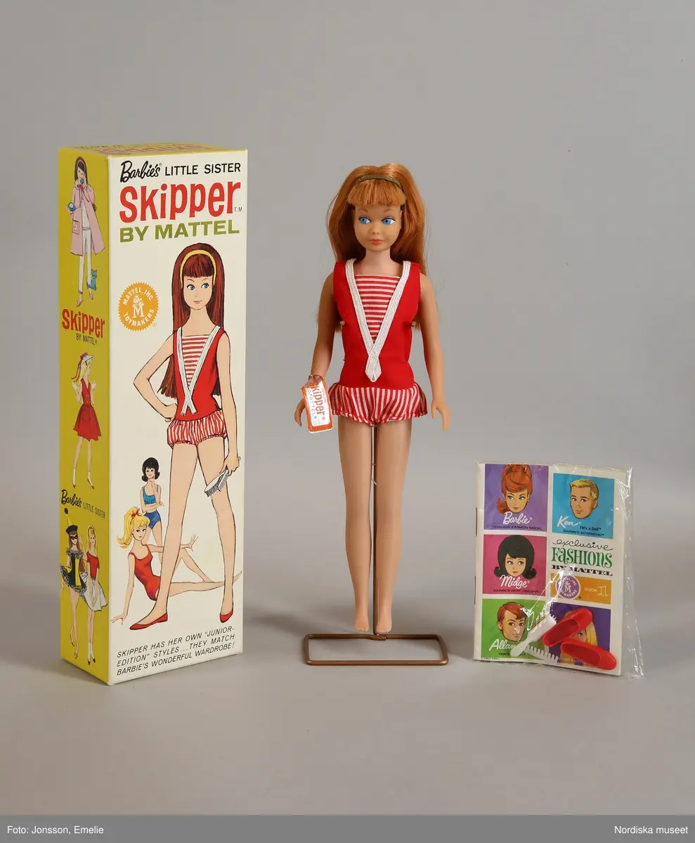 Inventering Sesam 1996-1999:
Barbiedocka, "Skipper" (a), i originalask, av plast, långt brunt hår, blå ögon. I förd röd hel sportdräkt med randiga byxor. I asken även ett par röda skor, 1 kam och en borste samt en katalog över Barbietillbehör (b). Skipper är Barbie's lillasyster. Dockan är amerikansk men tillverkad i Japan.
ELB maj 1967 /= Eva Lis Bjurman/