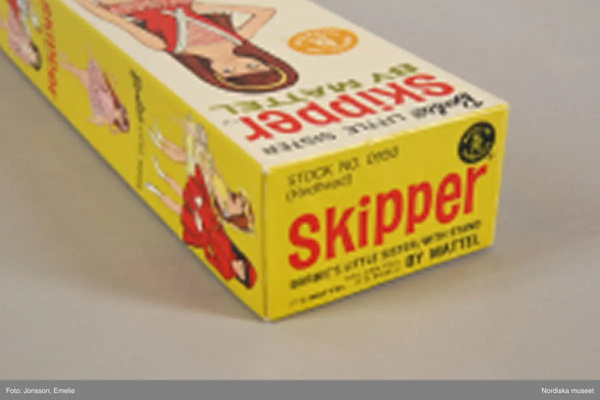 Inventering Sesam 1996-1999:
Barbiedocka, "Skipper" (a), i originalask, av plast, långt brunt hår, blå ögon. I förd röd hel sportdräkt med randiga byxor. I asken även ett par röda skor, 1 kam och en borste samt en katalog över Barbietillbehör (b). Skipper är Barbie's lillasyster. Dockan är amerikansk men tillverkad i Japan.
ELB maj 1967 /= Eva Lis Bjurman/