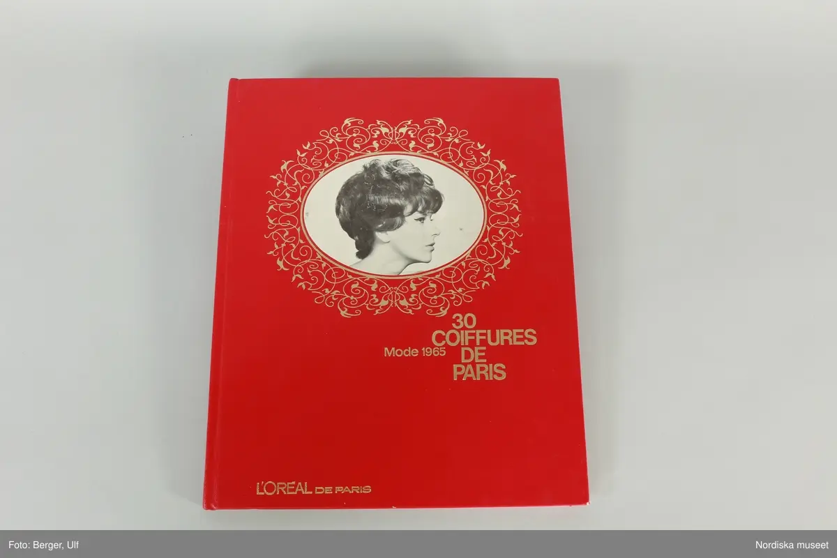 Huvudliggaren:
"a-b.
Album, 2 st, med modefrisyrer; a) röda pärmar, ovalt foto av kvinna; i guldfärg '30 Coiffures de Paris, Mode 1965 L' Oréal de Paris'; färg- och svartvita foton av 30 olika frisyrer; b) blå pärmar, grön dekor, text i vitt samma ss föreg., men från 1966. Mått 24,5 x 30,5 cm. Från Meeths skönhetssalong, Sthlm, 1965-66. G. 13/2 1970 av fröken Inga Lill Pehrsson, Stockholm."