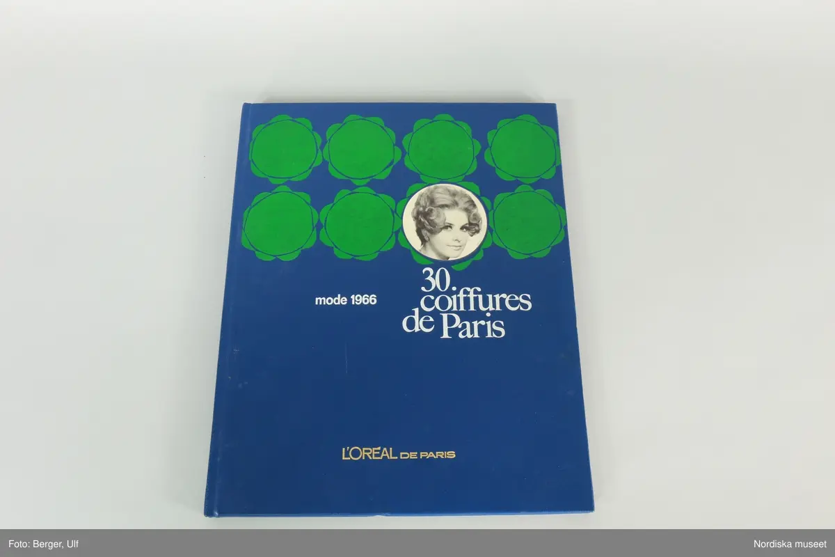 Huvudliggaren:
"a-b.
Album, 2 st, med modefrisyrer; a) röda pärmar, ovalt foto av kvinna; i guldfärg '30 Coiffures de Paris, Mode 1965 L' Oréal de Paris'; färg- och svartvita foton av 30 olika frisyrer; b) blå pärmar, grön dekor, text i vitt samma ss föreg., men från 1966. Mått 24,5 x 30,5 cm. Från Meeths skönhetssalong, Sthlm, 1965-66. G. 13/2 1970 av fröken Inga Lill Pehrsson, Stockholm."