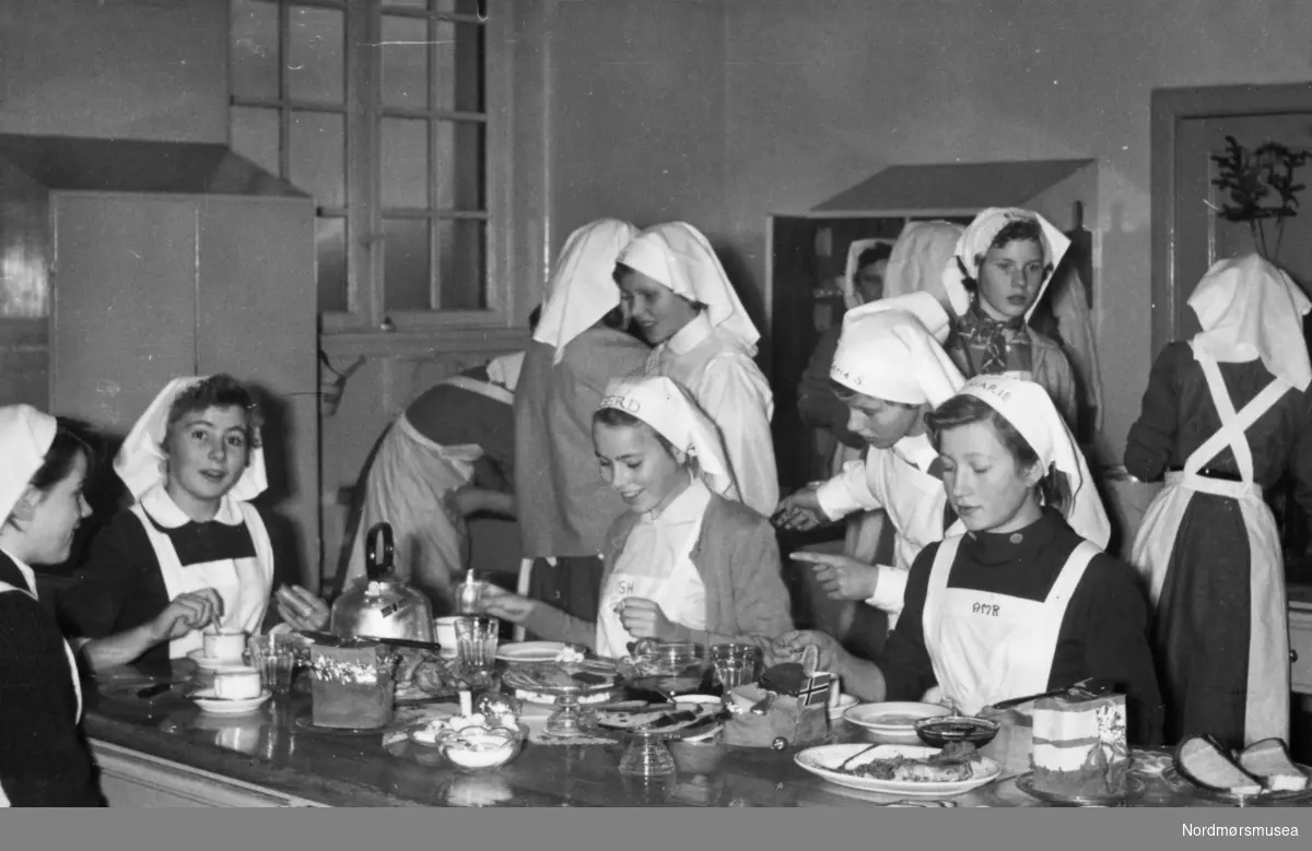 Påført tekst: "7. kl. 1957/58. På skolekjøkkenet." Arkivskaper av fotografiene KMb-2023-022.0012-0042 er Berit Trondsborg Røsberg og kommer fra Allanengen skole. Samlingen er gitt av Kristiansund skolemuseum/Kristiansund kommune.