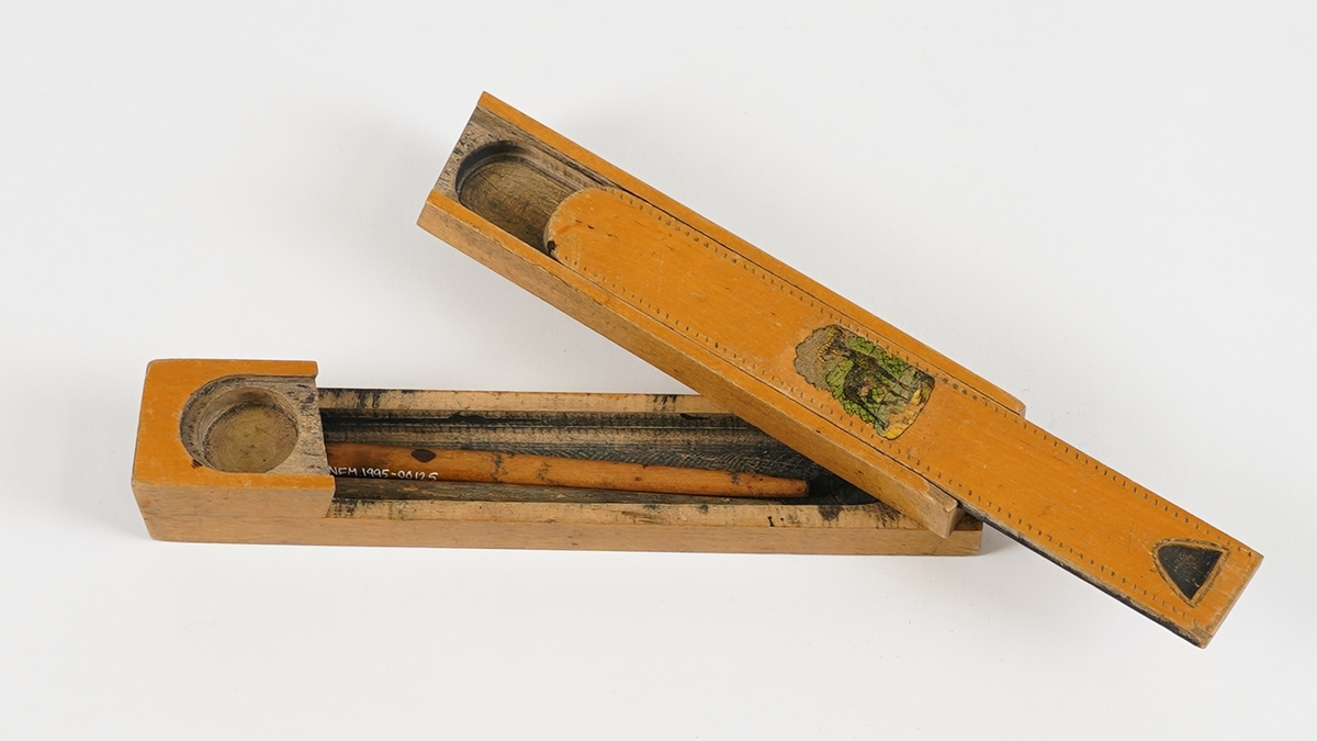 Penal med to rom. Det nedste rommet vert tilgjengeleg ved å svinge det øvste til sides. Det øvste rommet har skyvelok, og er delt i to rom. Skyveloket er avrunda i eine enden, og i den andre er det ei fordjuping som gjer det lettare å skyve loket fram og attende. Loket har stipla dekor rundt kanten, samt teikning av ein bukk midt på. I det nedste rommet ligg det to penneskaft, utan spissar. På innsida av loket er det set merke for kvar halve cm på eine langsida.