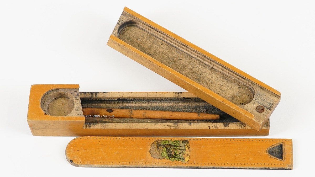 Penal med to rom. Det nedste rommet vert tilgjengeleg ved å svinge det øvste til sides. Det øvste rommet har skyvelok, og er delt i to rom. Skyveloket er avrunda i eine enden, og i den andre er det ei fordjuping som gjer det lettare å skyve loket fram og attende. Loket har stipla dekor rundt kanten, samt teikning av ein bukk midt på. I det nedste rommet ligg det to penneskaft, utan spissar. På innsida av loket er det set merke for kvar halve cm på eine langsida.