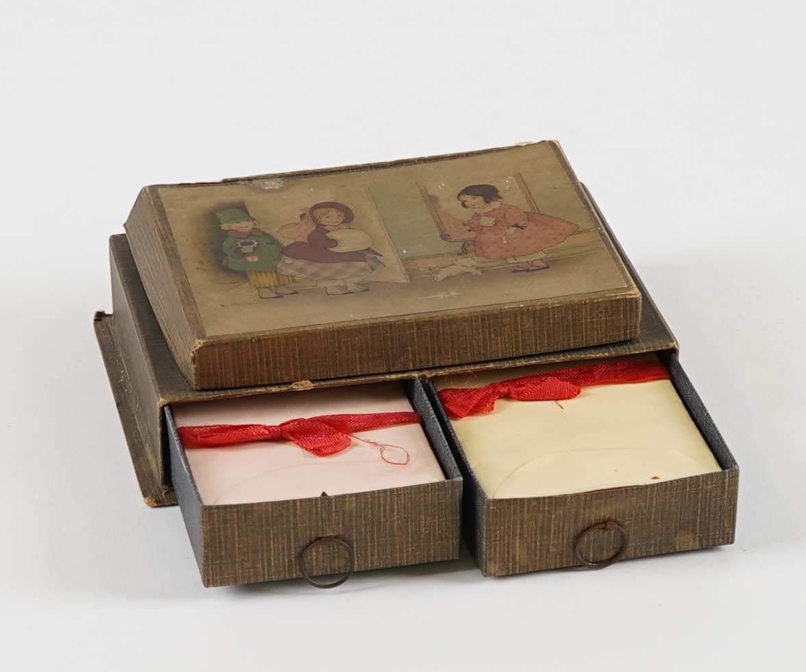 Ei rektangulær øskje med tre rom; to skuffer nedst og ei flat øskje på toppen. I skuffene er det små papirkonvoluttar med raudt band rundt, og i toppen er det små, linjerte ark. I øskja på toppen er det òg diverse små "skattar"; eit teikna portrett, eit utklypt bilete av ein påfugl, eit lite perlearmband (+to lause perler), nokre små korallbitar og ein kalendarlapp (Oktober 12 Søndag). På loket på toppen er det bilete av tre dokkeliknande figurar, og ein liten hund.