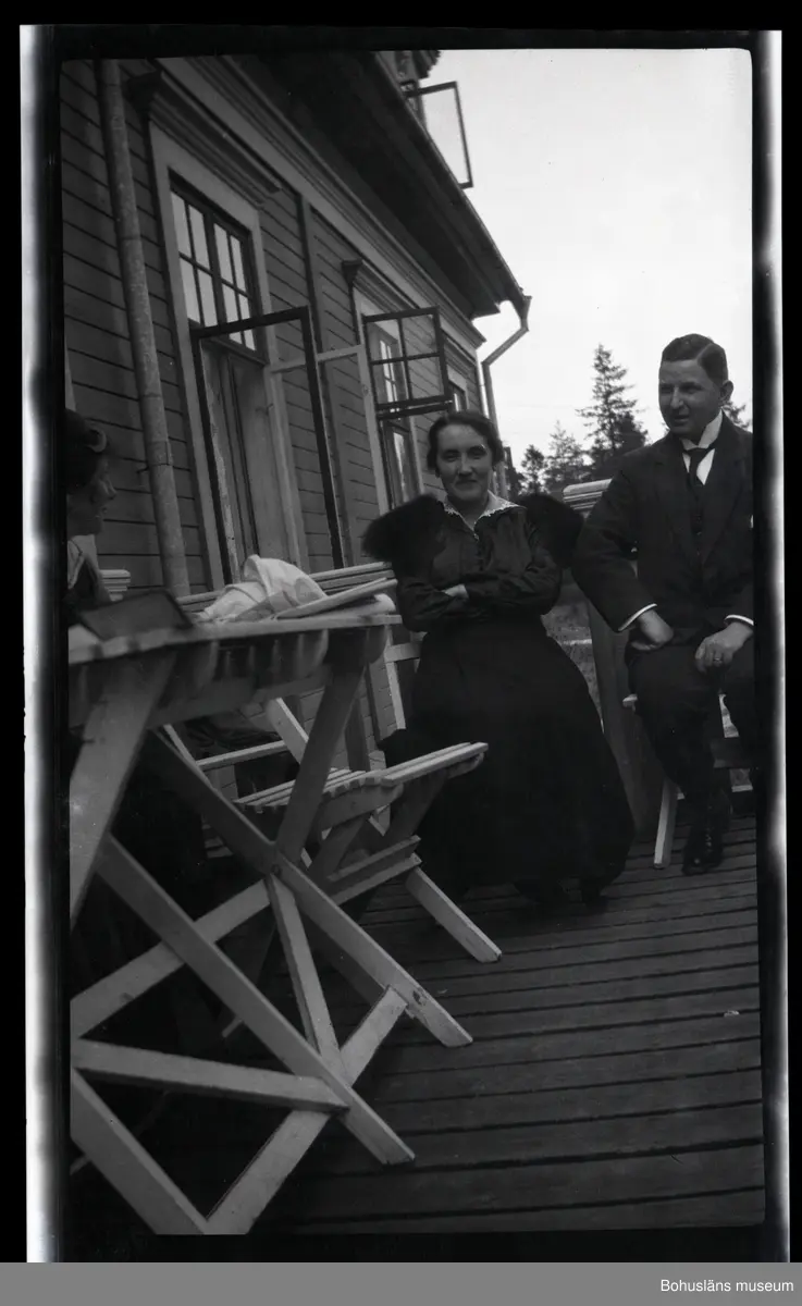 Tre personer sittandes vid bord utanför ett hus.