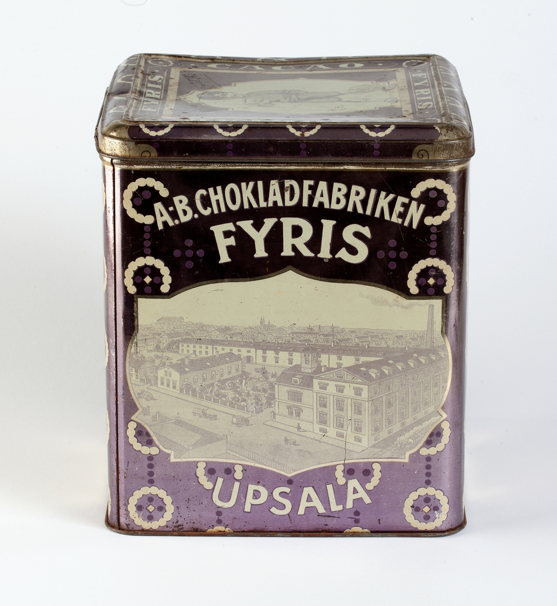 Burk av järnplåt, målad i ljuslila med dekor i vitt. Text "A-B. Chokladfabriken Fyris Upsala".