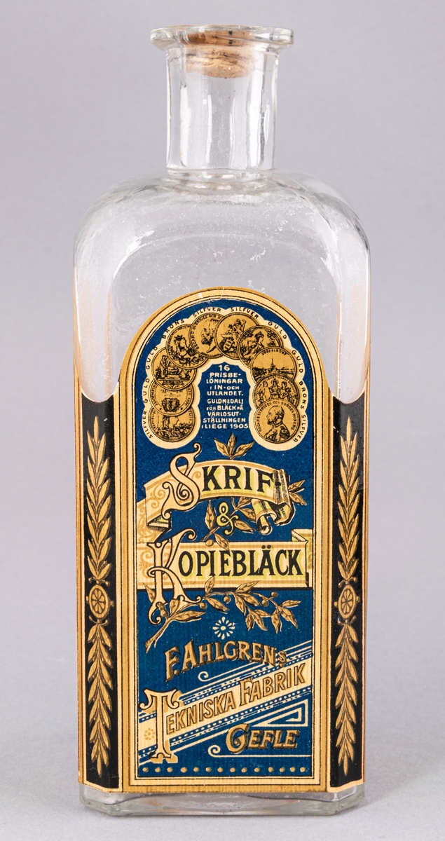Glasflaska för bläck, fyrkantig med kork. Etikett på tre sidor, "Skrif- & Kopiebläck", "F. Ahlgrens Tekniska Fabrik Gefle".