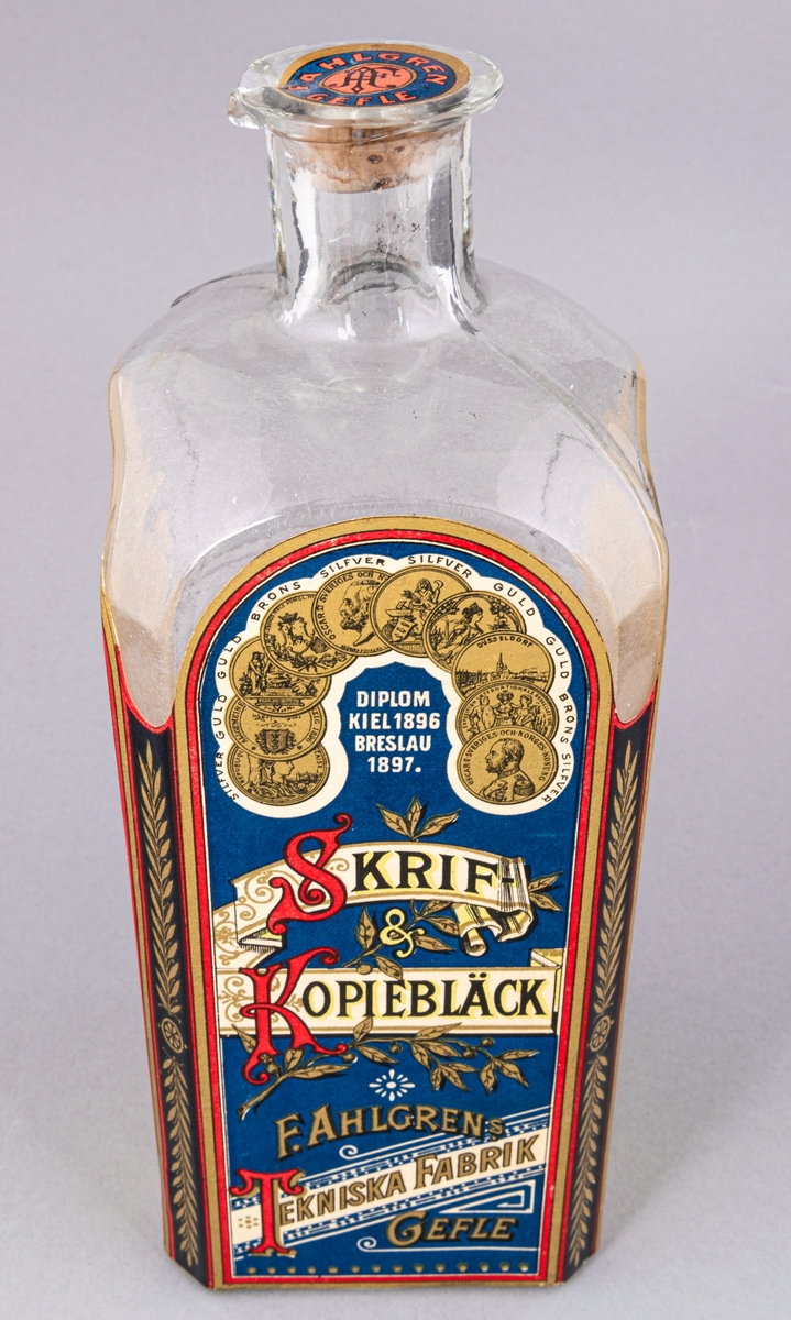 Glasflaska med kork innehållande bläck. Flaskan fyrsidig. Etikett med text "Skrif- & Kopiebläck" på framsidan.