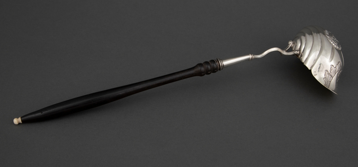 Punsjeøse i sølv med skaft av mørkt løvtre med knapp av ben eller elfenben. Den ovale skålen er innvendig forgylt og har et skjenkenebb på tvers av skaftets retning. Skålen har drevne riller og dekor i lavt relieff.