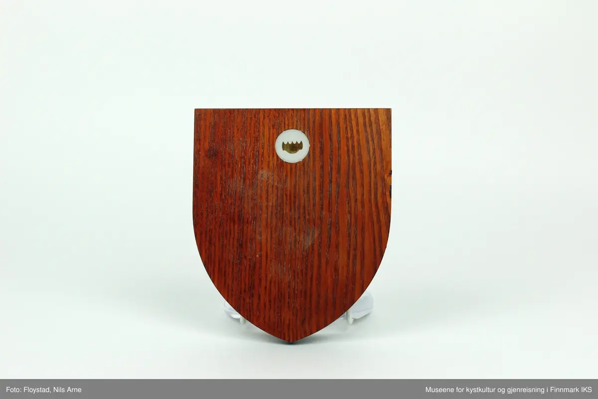 Et våpenskjold dekorert med logoen til The Royal North Cape Club (RNCC). 

Skjoldet har en trekantformet trebase av tresorten ask og er impregnert med mørk beis. Midt på skjoldet er logoen til The Royal North Cape Club limt på. Logoen er også skjært ut av tre og malt i fargene gul, rød og gull. På baksiden er det skjært ut et hull med et feste for oppheng laget av plast. På feste står det "MADE IN GREAT BRITAIN". 

Våpenskjoldet ligger i en blå eske og på lokket og den ene siden er det trykt logoen til produsenten GK Beaulah & Co LTD. På baksiden er det trykt opplysninger om hvilke produkter firmaet lager.