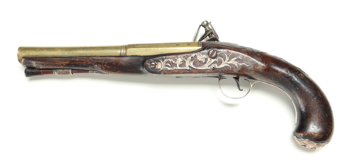 Flintlåspistol med helstock och lås i stål i s.k. Centuckystil. Pipan är gjord i mässing, och kolvkappa, varbygel, sidobleck, tumplåt och rörkor i silver. Pipan är märkt "ST-965", samt två kontrollstämplar från London, och som är åttakantig i formen, men övergår i cylindrisk form ut mot mynningen. Kolvkappan har silverstämplar från Birmingham, varbygeln likaså. Sidoblecket är utformat som blomsterslingor, och kolvkappan som en maskaron. Varbygeln är ornamenterad med en blomma i en oval. Längst fram är den utformad som ett ekollon. Tumplåten är märkt med "EC". Laddstock finns under framstocken.
Inskrivet i huvudkatalogen 1974.
