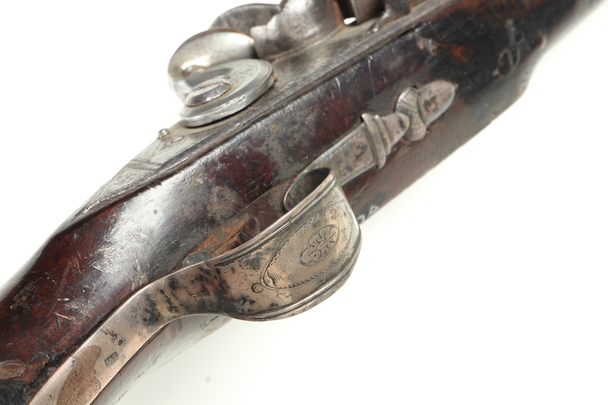 Flintlåspistol med helstock och lås i stål i s.k. Centuckystil. Pipan är gjord i mässing, och kolvkappa, varbygel, sidobleck, tumplåt och rörkor i silver. Pipan är märkt "ST-965", samt två kontrollstämplar från London, och som är åttakantig i formen, men övergår i cylindrisk form ut mot mynningen. Kolvkappan har silverstämplar från Birmingham, varbygeln likaså. Sidoblecket är utformat som blomsterslingor, och kolvkappan som en maskaron. Varbygeln är ornamenterad med en blomma i en oval. Längst fram är den utformad som ett ekollon. Tumplåten är märkt med "EC". Laddstock finns under framstocken.
Inskrivet i huvudkatalogen 1974.