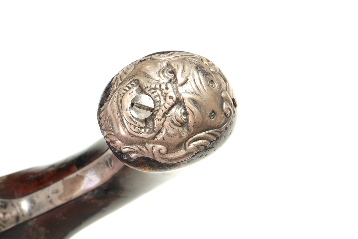 Flintlåspistol med helstock och lås i stål i s.k. Centuckystil. Pipan är gjord i mässing, och kolvkappa, varbygel, sidobleck, tumplåt och rörkor i silver. Pipan är märkt "ST-965", samt två kontrollstämplar från London, och som är åttakantig i formen, men övergår i cylindrisk form ut mot mynningen. Kolvkappan har silverstämplar från Birmingham, varbygeln likaså. Sidoblecket är utformat som blomsterslingor, och kolvkappan som en maskaron. Varbygeln är ornamenterad med en blomma i en oval. Längst fram är den utformad som ett ekollon. Tumplåten är märkt med "EC". Laddstock finns under framstocken.
Inskrivet i huvudkatalogen 1974.