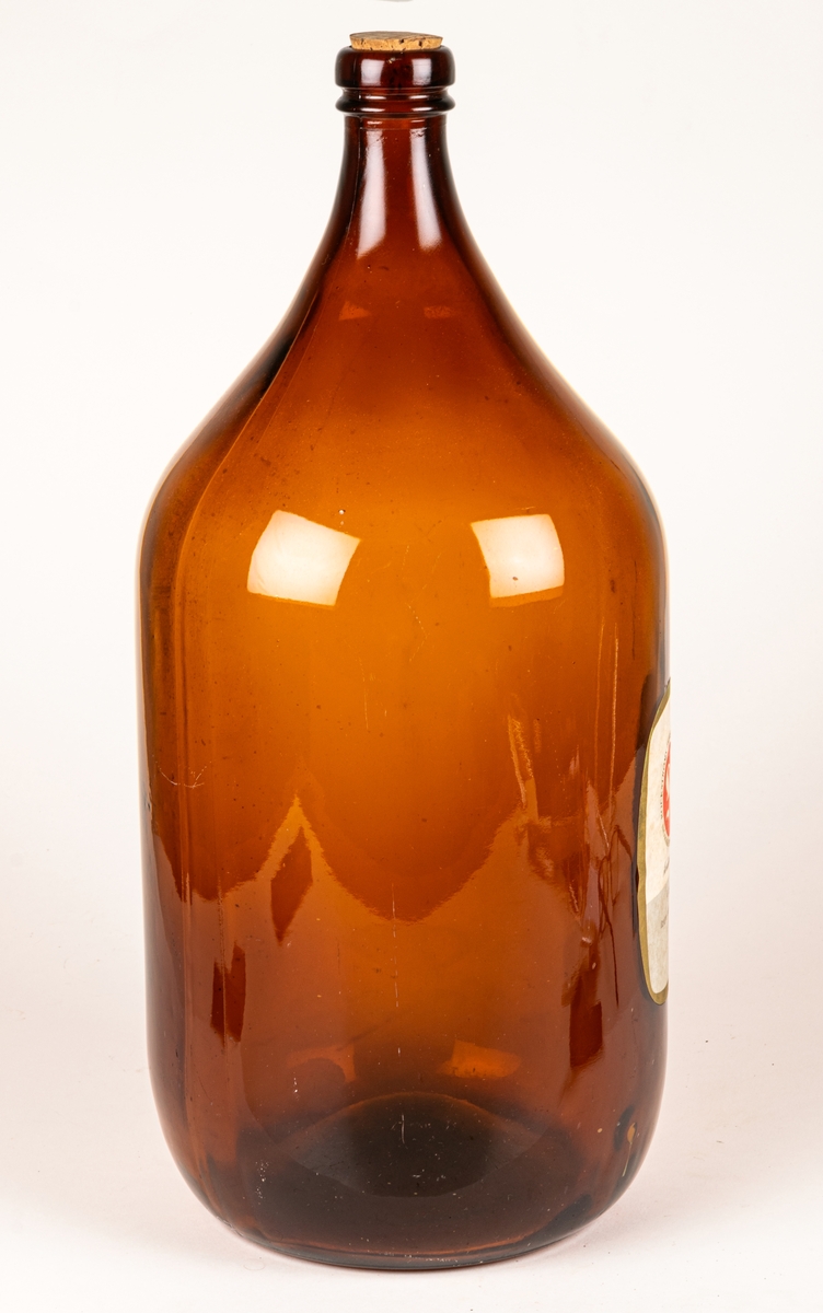 Brun glasflaska. Rektangulär grå och vit etikett med guldkant. Rött sigill med vitt "R", text runt sigillet: "ROCKSTRÖMS FABRIKER AKTIEBOLAG NORRKÖPING SWEDEN" samt "KVALITETSMÄRKET 8 KG GRAPE ESSENS 758."