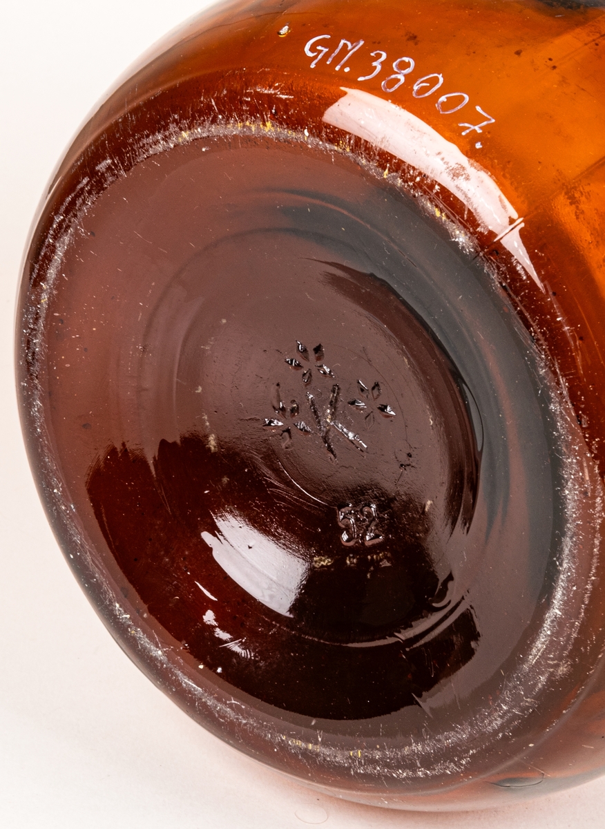 Brun glasflaska. Rektangulär grå och vit etikett med guldkant. Rött sigill med vitt "R", text runt sigillet: "ROCKSTRÖMS FABRIKER AKTIEBOLAG NORRKÖPING SWEDEN" samt "KVALITETSMÄRKET 8 KG GRAPE ESSENS 758."