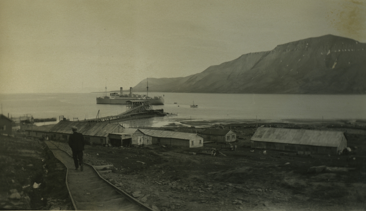 Et skip på vei til kaia i Longyearbyen. Mann går langs skinnegangen.