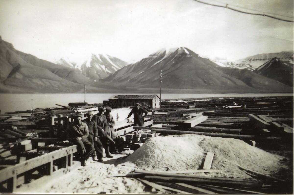 Bygging av sagbruket i Longyearbyen. Johan E Dyrendahl (står lengst bak ved sagbenken) fra Rissa i Nord-Trøndelag, kom i 1949 til Svalbard sammen med Parelius Rossvold og Gunnar Holten (også fra Rissa) for å sluttføre bygginga av saga i Longyearbyen Se også skriftlige opplysninger: Boks 99, mappe 5, i fjernarkiv.