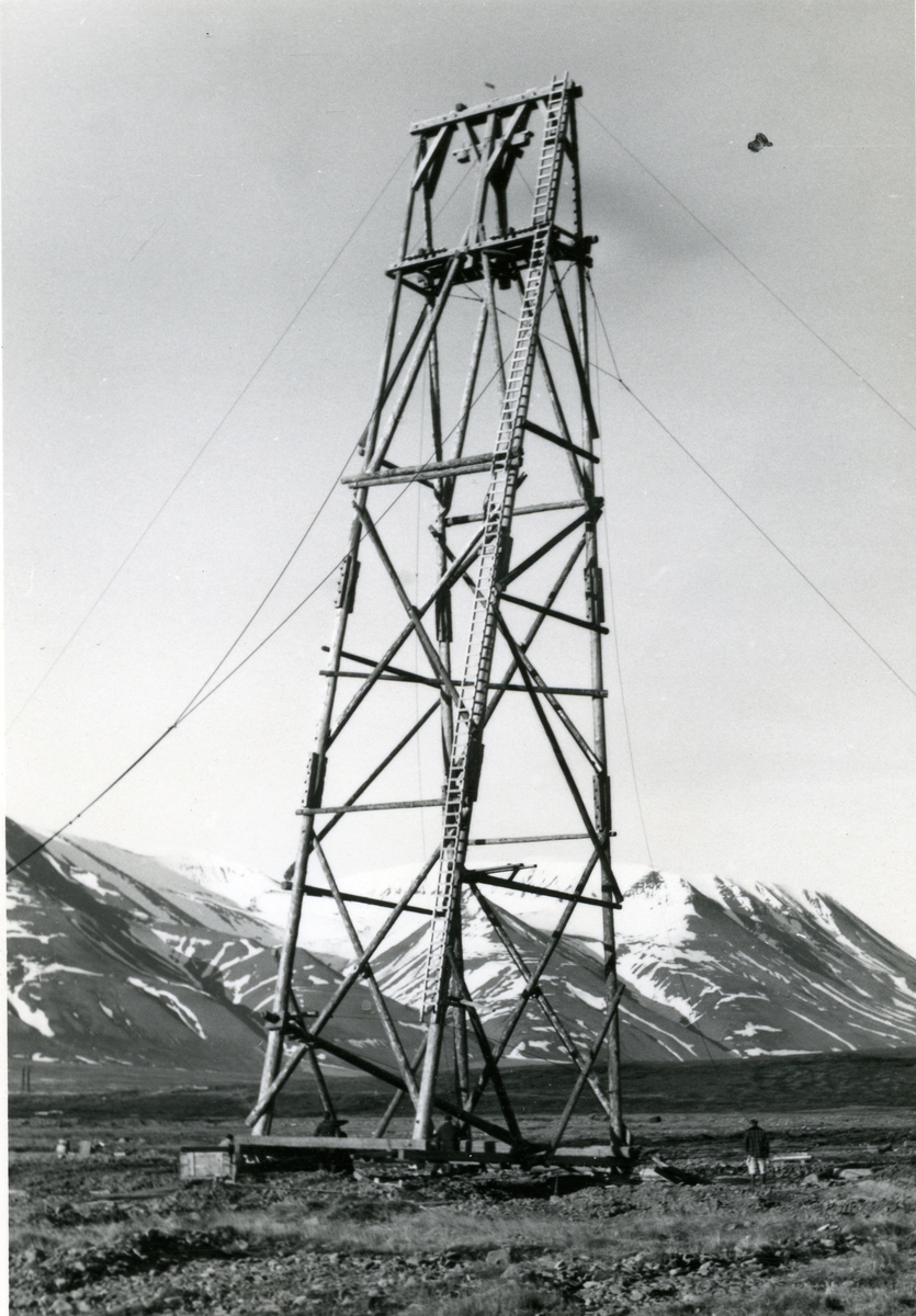 Reising av taubanebukk i Longyeardalen.Taubanetrasèen til gruve 5 bygges sommeren 1959. Dette var den høyeste bukken på banen til Gruve 5. Den ble reist ved hjelp avto bulldosere med wire og spill. En reiste og en holdt igjen. Så ble bukken senket ned ved hjelp av jekker. Bulldoserkjørerne var Tor Kristoffersen og Kåre G. Pedersen. Samme motiv som SVF 13081, tatt av Erling Nødtvedt. Kan være en kopi. 2 eks.