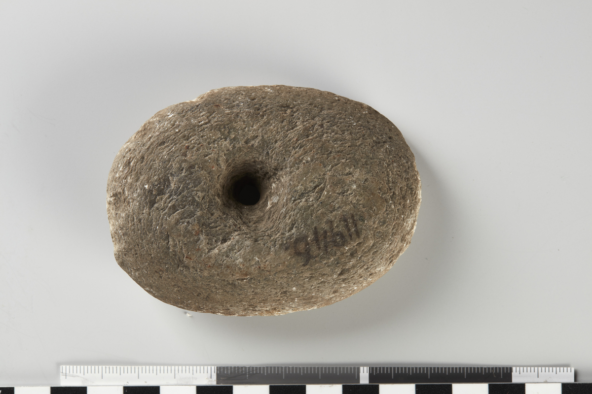 Hammer af Sten, lig NO. 46, meget liden og beskadiget paa den ene Side, 8,5 cm. lang. Hullet meget trangt i Midten, maaske ufuldendt.
F. i Vang Pgd., Valders. 