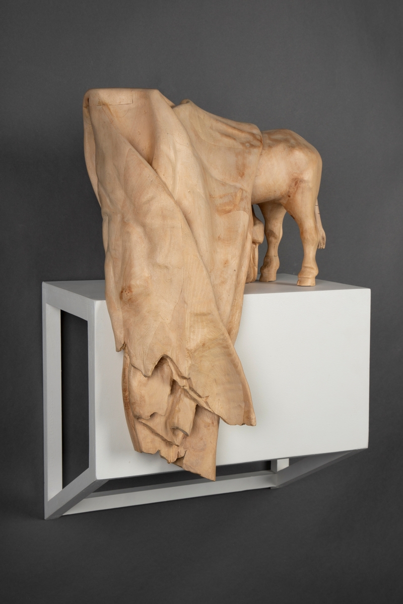 Treskulptur av en ku foldet inn i et tøystykke.