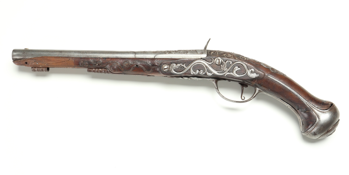 Flintlåspistol med helstock i valnöt. Pipan, varbygeln, tumplåten och sidoplåten är i ciselerad stål med upphöjda ornament. På låsblecket är namnet Willem van Essen graverat. Även framstocken har utsirade ornament i relief. Här finns även en spetsrörka och en överrörka, även dessa i stål. Kolvkappan, i stål, är försedd med en kolvknapp iform av en maskaron, omgärdad av ett slingmönster. Pipan är slätborrad, och här finns ett litet mässingskorn längst ut vid mynningen.
Inskrivet i huvudkatalogen 1869.