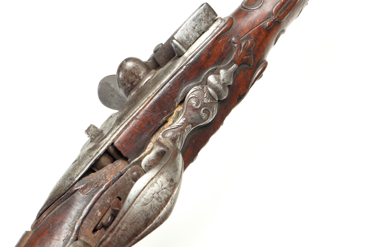 Flintlåspistol med helstock i valnöt. Pipan, varbygeln, tumplåten och sidoplåten är i ciselerad stål med upphöjda ornament. På låsblecket är namnet Willem van Essen graverat. Även framstocken har utsirade ornament i relief. Här finns även en spetsrörka och en överrörka, även dessa i stål. Kolvkappan, i stål, är försedd med en kolvknapp iform av en maskaron, omgärdad av ett slingmönster. Pipan är slätborrad, och här finns ett litet mässingskorn längst ut vid mynningen.
Inskrivet i huvudkatalogen 1869.