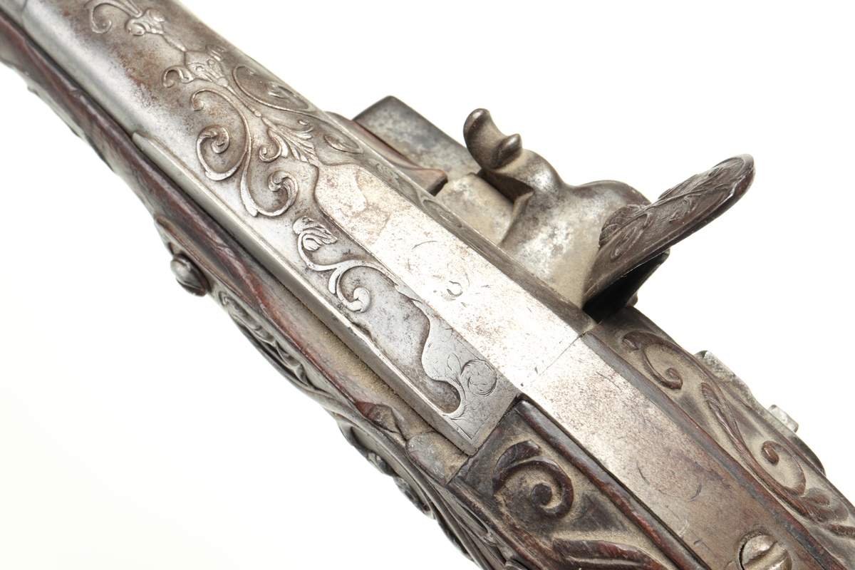 Flintlåspistol med helstock i valnöt. Pipan, varbygeln, tumplåten och sidoplåten är i ciselerad stål med upphöjda ornament. På låsblecket är namnet Willem van Essen graverat. Även framstocken har utsirade ornament i relief. Här finns även en spetsrörka och en överrörka, även dessa i stål. Kolvkappan, i stål, är försedd med en kolvknapp iform av en maskaron, omgärdad av ett slingmönster. Pipan är slätborrad, och här finns ett litet mässingskorn längst ut vid mynningen.
Inskrivet i huvudkatalogen 1869.