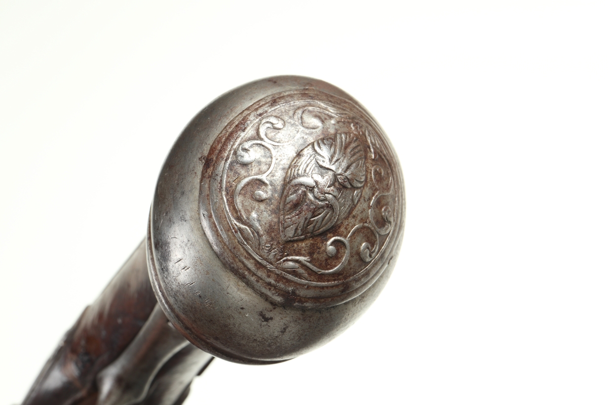 Flintlåspistol med helstock i valnöt. Pipan, varbygeln, tumplåten och sidoplåten är i ciselerad stål med upphöjda ornament. På låsblecket är namnet Willem van Essen graverat. Även framstocken har utsirade ornament i relief. Här finns även en spetsrörka och en överrörka, även dessa i stål. Kolvkappan, i stål, är försedd med en kolvknapp iform av en maskaron, omgärdad av ett slingmönster. Pipan är slätborrad, och här finns ett litet mässingskorn längst ut vid mynningen.
Inskrivet i huvudkatalogen 1869.