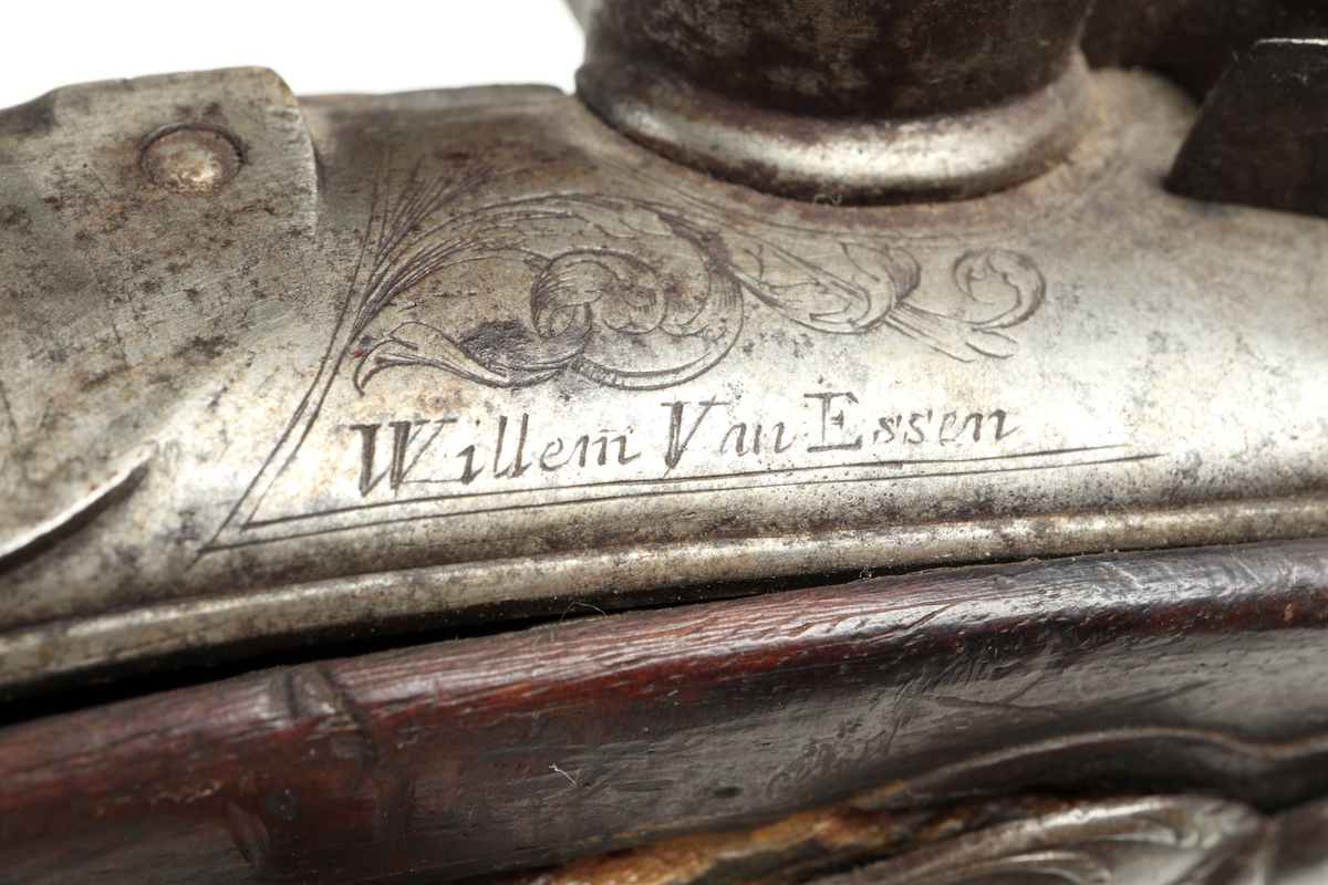 Flintlåspistol med helstock i valnöt. Pipan, varbygeln, tumplåten och sidoplåten är i ciselerad stål med upphöjda ornament. På låsblecket är namnet Willem van Essen graverat. Även framstocken har utsirade ornament i relief. Här finns även en spetsrörka och en överrörka, även dessa i stål. Kolvkappan, i stål, är försedd med en kolvknapp iform av en maskaron, omgärdad av ett slingmönster. Pipan är slätborrad, och här finns ett litet mässingskorn längst ut vid mynningen.
Inskrivet i huvudkatalogen 1869.