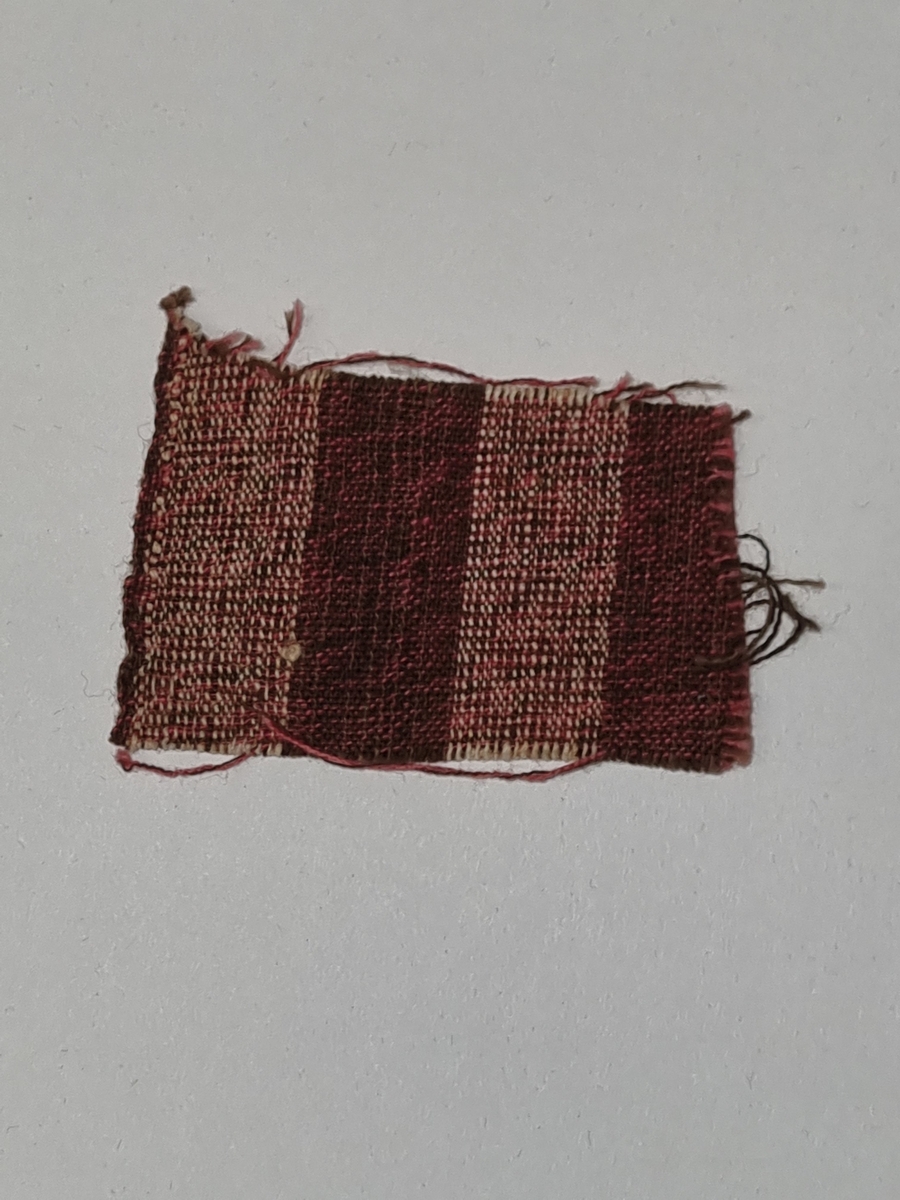 Én stoffprøve, vevd. (del av samling av stoffrester av ulike stoffer, oppbevart i eske av kartong)