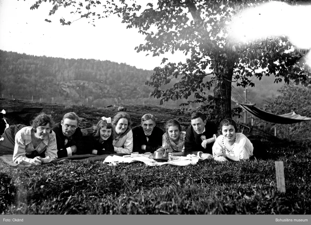 Åtta personer liggandes på filtar i en trädgård med uppdukad picknick.