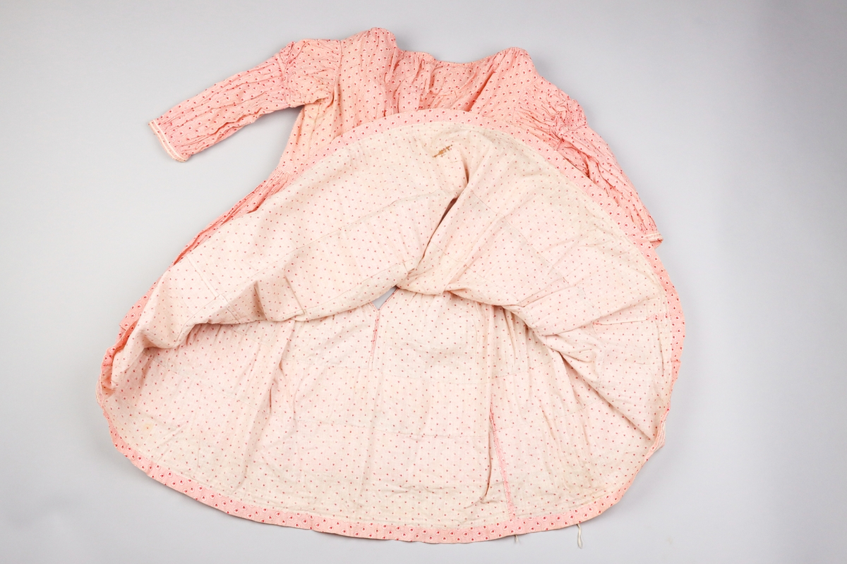 Barnklänning av tät och tunn bomullsväv med tryckt mönster i rosa, rött och vitt. Mönstret föreställer ett litet löv i en cirkel, vilken upprepas som täta prickar mot en rosa botten.

Halsringningen är vid och har en dragsko för reglering. Klänningens liv är rynkat i partier mot midjan. På insidan är ett band påsytt ca 4 cm upp från midjan för att samla ihop rynkorna både på fram och bakstycken. Klänningens liv är fodrat med oblekt bomullsväv som har en isättning i form av en kil mitt fram, troligen för att öka storleken. Klänningens livfoder stängs med hyskor och hakar i mässingstråd och järntråd i en knäppning mitt bak. Knäppningen döljs av de samlade vecken på livets baksida. Veckens band och halsringningens band knyts bak.

Ärmarna är rynkade i en puff närmast axeln. Den del av ärmen har ett orynkat slätt foder av oblekt bomullstyg. Puffärmen har en egen ärmlinning och den längre ärmen med mindre omfång är fäst innuti den. Den längre ärmen är inte fodrad. Det verkar som om den delen av ärmen kan sprättas av för att ändra klänningen till kortärmad. Den nedre ärmen är samlad mot en ärmlinning dekorerad med två parallella vita flätade bomullsband.

Klänningens kjol är veckad med parallella rynkor mot midjan och varje rynka är fäst mot livet med ett stygn. Kjolen öppnas med ett sprund mitt bak. Kjolen har två horisontella veck. Det övre är 6,5 cm djupt och det undre 5,6 cm djupt. Vecken ger kjolens vidd viss stadga, men kan också ha använts för att reglera längden. Kjolens nedre kant är uppvikt och fållad med fållstygn. Längs nederkanten löper tre parallella vita flätade bomulsband.

Hela plagget är handsytt med exempel på flera olika typer av stygn och sömnadstekniker. Fodret i livet har flera revor vilket möjliggör studier av insidan.