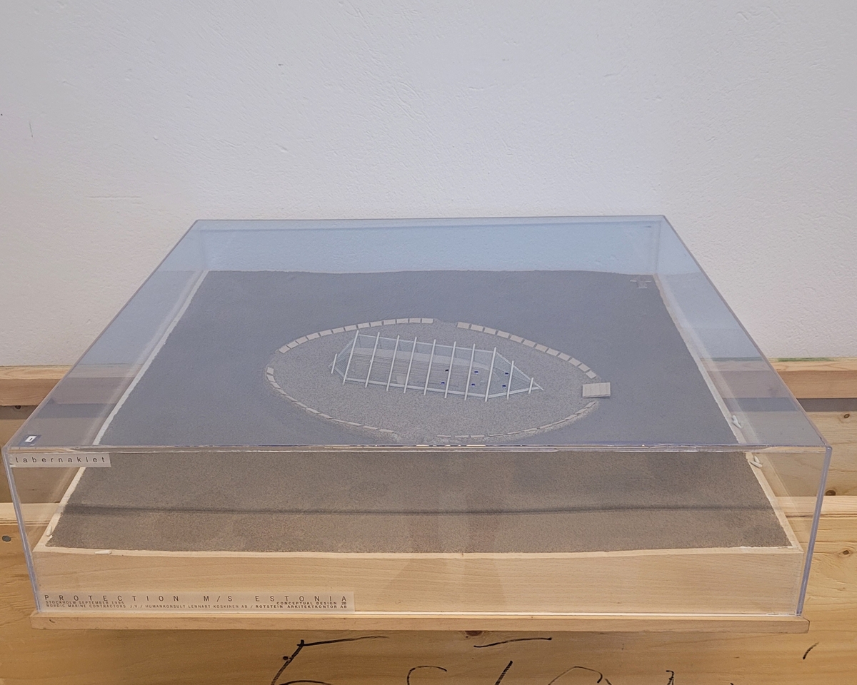 "Tabernaklet". Modell till alternativ för den planerade övertäckningen av vraket M/S Estonia. Modellen är utförd i september 1995. Modellen är placerad på träplatta med plexiglashuv.
6 hål, 3+3 parallellt, i plexihuvens tak illustrerar hur bojar var tänkta att märka ut platsen.