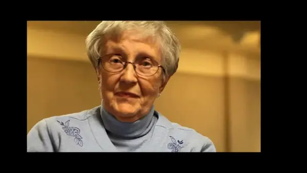 Foto fra filmen, Eldre kvinne med briller, kort grått hår og lyseblå trøye