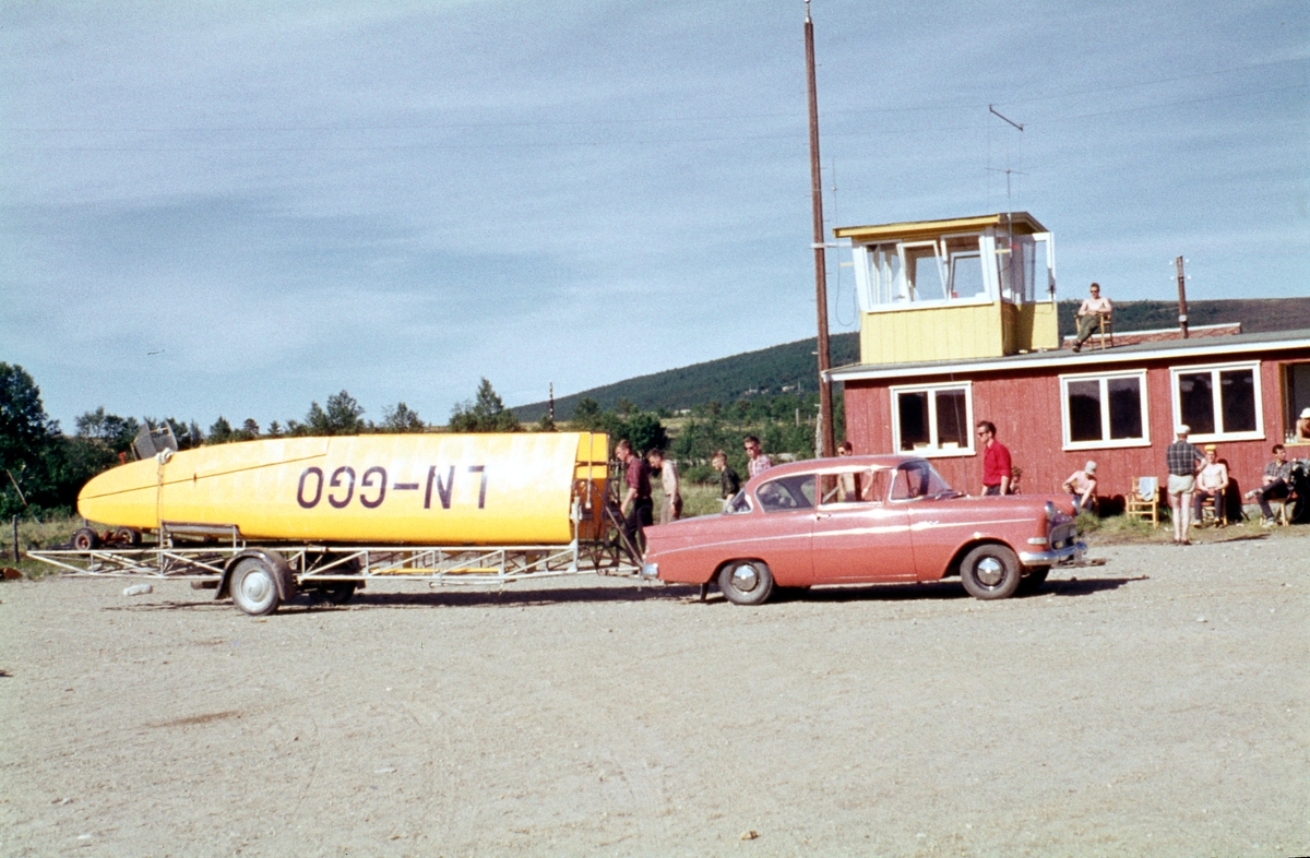 Trondheim Fk.s Baby IIB lastet på henger. Bak ses Røros flyplass første ekspedisjonsbygg. Flyklubbene i Trondheim flyttet kursene sine fra Øysand til Røros flyplass i 1962.
