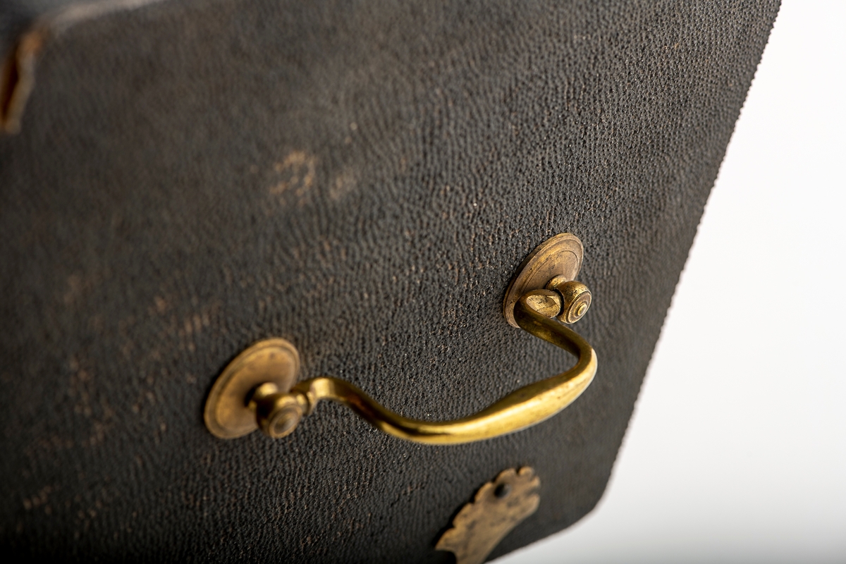 Trepanasjonsbestikk i etui.
Etui trukket med sort prikket  papp,  messing  beslag og messinghank midt på  lokket, med nøkkel i snor, innv. rød  fløyel, malt rødt langs kantene.

Inneolder 12 kirurgiske instrumenter,  derav seks med palisander (det ene  er skaft til 3 instrumenter), og en barberkniv med skilpaddeskaft. Tang med ukjent stempel.