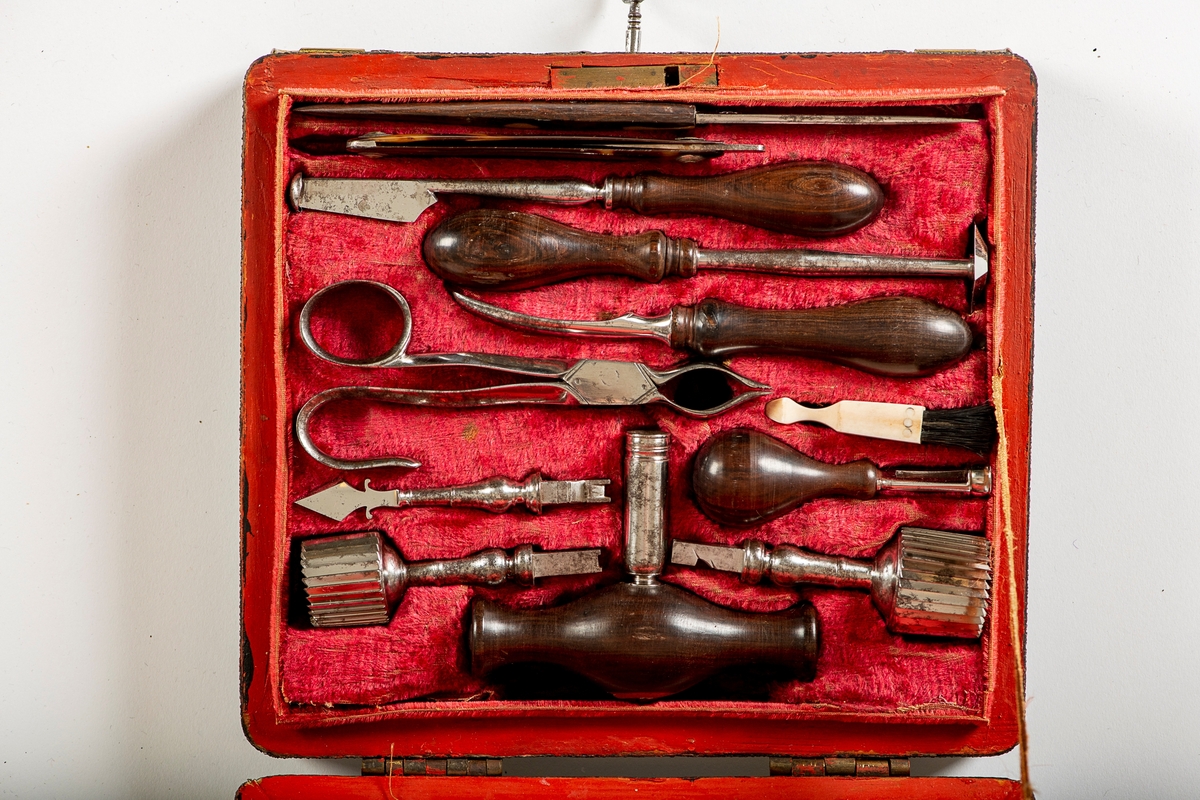 Trepanasjonsbestikk i etui.
Etui trukket med sort prikket  papp,  messing  beslag og messinghank midt på  lokket, med nøkkel i snor, innv. rød  fløyel, malt rødt langs kantene.

Inneolder 12 kirurgiske instrumenter,  derav seks med palisander (det ene  er skaft til 3 instrumenter), og en barberkniv med skilpaddeskaft. Tang med ukjent stempel.