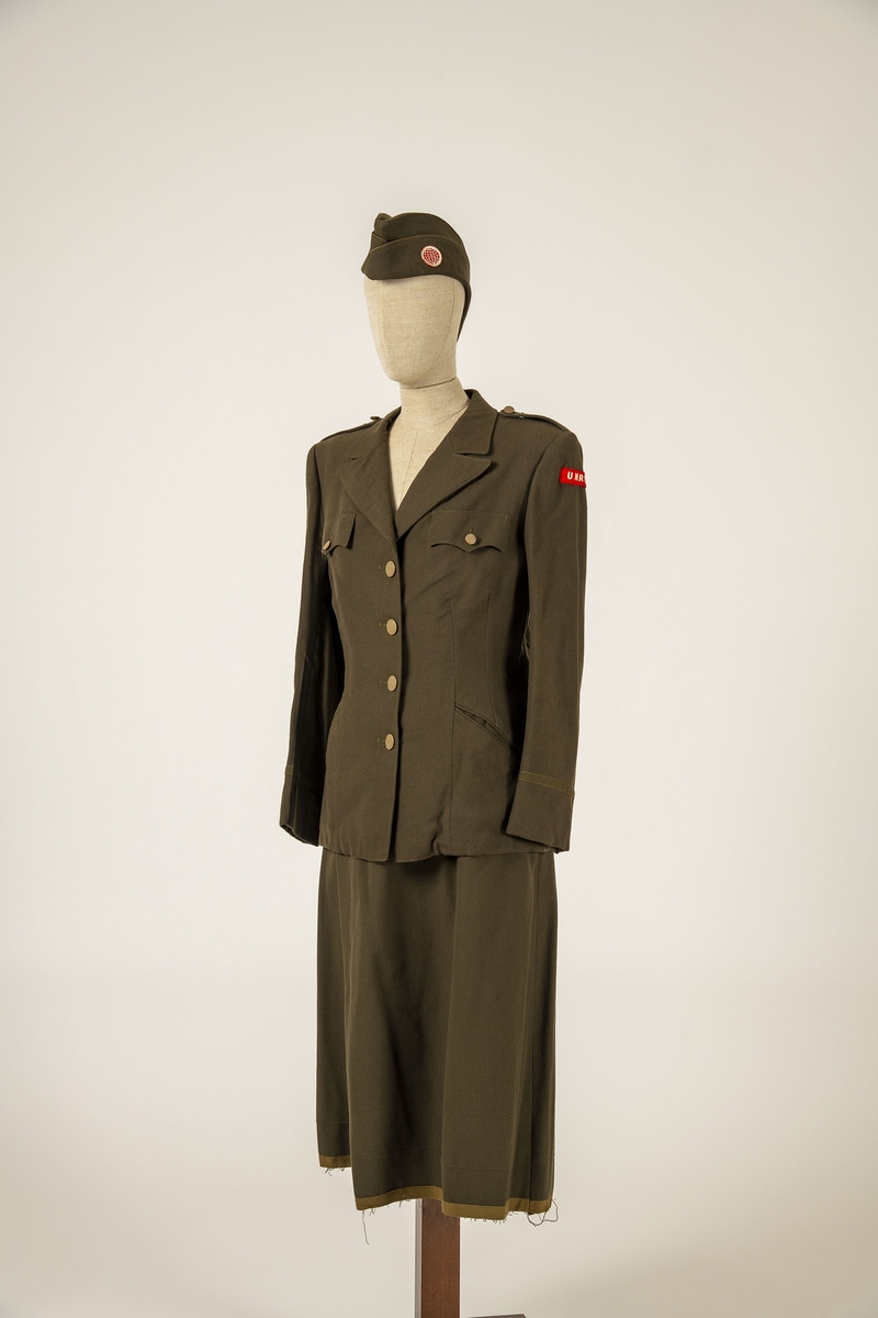 Uniform i flere deler:
a) Jakke. Påsydd rødt merke på ventre skulder:  UNRRA. Etikett i nakken: Size 18 R. En stripe rundt ermene, enkeltspent, brystlommer og to innstikklommer. Krage og slag. Skulderklaffer. Plastknapper.
b) Skjørt. Rett skjørt, midtsøm foran og bak. smal linning, glidelås i siden. Tilstand: falden tatt opp, brunt bendelbånd nederst. 
c) Båtlue. Brunt polyesterfor. Etikett: 23. Utvisket stempel i sølv. 
d) Et par sokker. Ull, militær brungrønn.Ribbestrikket, glatt hel og såle.
e-g) Tre lommetørklær. Bomull, militær brune.