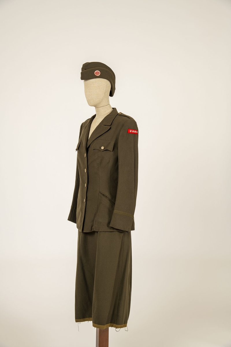 Uniform i flere deler:
a) Jakke. Påsydd rødt merke på ventre skulder:  UNRRA. Etikett i nakken: Size 18 R. En stripe rundt ermene, enkeltspent, brystlommer og to innstikklommer. Krage og slag. Skulderklaffer. Plastknapper.
b) Skjørt. Rett skjørt, midtsøm foran og bak. smal linning, glidelås i siden. Tilstand: falden tatt opp, brunt bendelbånd nederst. 
c) Båtlue. Brunt polyesterfor. Etikett: 23. Utvisket stempel i sølv. 
d) Et par sokker. Ull, militær brungrønn.Ribbestrikket, glatt hel og såle.
e-g) Tre lommetørklær. Bomull, militær brune.