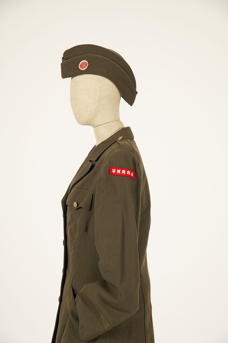 Uniform i flere deler:
a) Jakke. Påsydd rødt merke på ventre skulder:  UNRRA. Etikett i nakken: Size 18 R. En stripe rundt ermene, enkeltspent, brystlommer og to innstikklommer. Krage og slag. Skulderklaffer. Plastknapper.
b) Skjørt. Rett skjørt, midtsøm foran og bak. smal linning, glidelås i siden. Tilstand: falden tatt opp, brunt bendelbånd nederst. 
c) Båtlue. Brunt polyesterfor. Etikett: 23. Utvisket stempel i sølv. 
d) Et par sokker. Ull, militær brungrønn.Ribbestrikket, glatt hel og såle.
e-g) Tre lommetørklær. Bomull, militær brune.