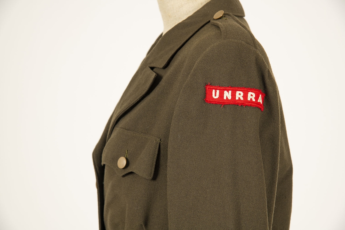 Uniform i flere deler:
a) Jakke. Påsydd rødt merke på ventre skulder:  UNRRA. Etikett i nakken: Size 18 R. En stripe rundt ermene, enkeltspent, brystlommer og to innstikklommer. Krage og slag. Skulderklaffer. Plastknapper.
b) Skjørt. Rett skjørt, midtsøm foran og bak. smal linning, glidelås i siden. Tilstand: falden tatt opp, brunt bendelbånd nederst. 
c) Båtlue. Brunt polyesterfor. Etikett: 23. Utvisket stempel i sølv. 
d) Et par sokker. Ull, militær brungrønn.Ribbestrikket, glatt hel og såle.
e-g) Tre lommetørklær. Bomull, militær brune.