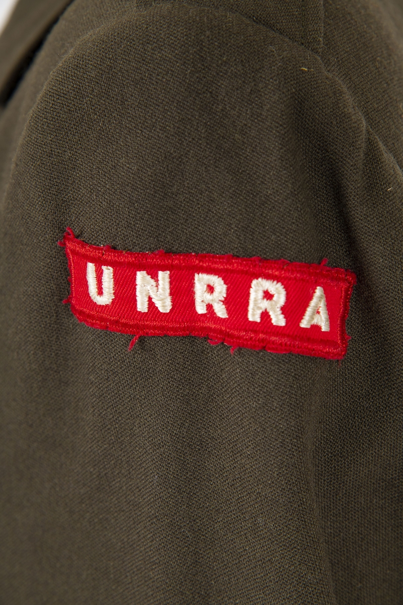 Uniform i flere deler:
a) Jakke. Påsydd rødt merke på ventre skulder:  UNRRA. Etikett i nakken: Size 18 R. En stripe rundt ermene, enkeltspent, brystlommer og to innstikklommer. Krage og slag. Skulderklaffer. Plastknapper.
b) Skjørt. Rett skjørt, midtsøm foran og bak. smal linning, glidelås i siden. Tilstand: falden tatt opp, brunt bendelbånd nederst. 
c) Båtlue. Brunt polyesterfor. Etikett: 23. Utvisket stempel i sølv. 
d) Et par sokker. Ull, militær brungrønn.Ribbestrikket, glatt hel og såle.
e-g) Tre lommetørklær. Bomull, militær brune.
