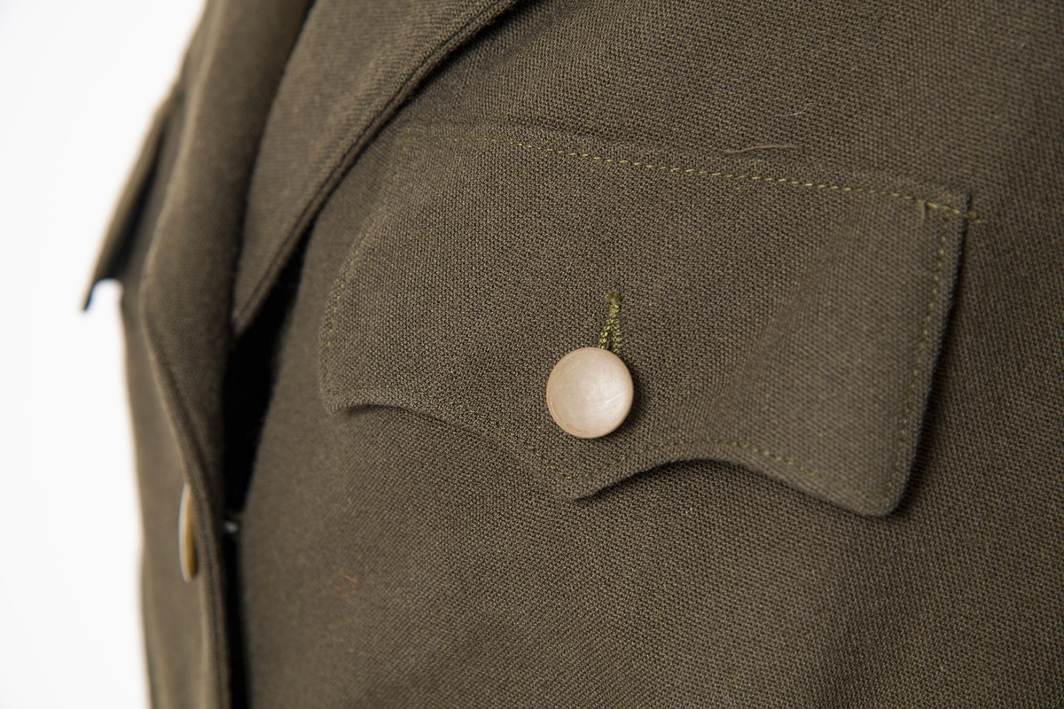 Uniform i flere deler:
a) Jakke. Påsydd rødt merke på ventre skulder:  UNRRA. Etikett i nakken: Size 18 R. En stripe rundt ermene, enkeltspent, brystlommer og to innstikklommer. Krage og slag. Skulderklaffer. Plastknapper.
b) Skjørt. Rett skjørt, midtsøm foran og bak. smal linning, glidelås i siden. Tilstand: falden tatt opp, brunt bendelbånd nederst. 
c) Båtlue. Brunt polyesterfor. Etikett: 23. Utvisket stempel i sølv. 
d) Et par sokker. Ull, militær brungrønn.Ribbestrikket, glatt hel og såle.
e-g) Tre lommetørklær. Bomull, militær brune.